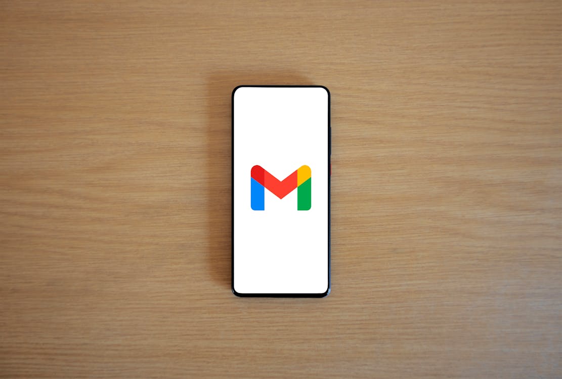 Free A smartphone displaying the Gmail app logo on a wooden surface, viewed from above. Stock Photo